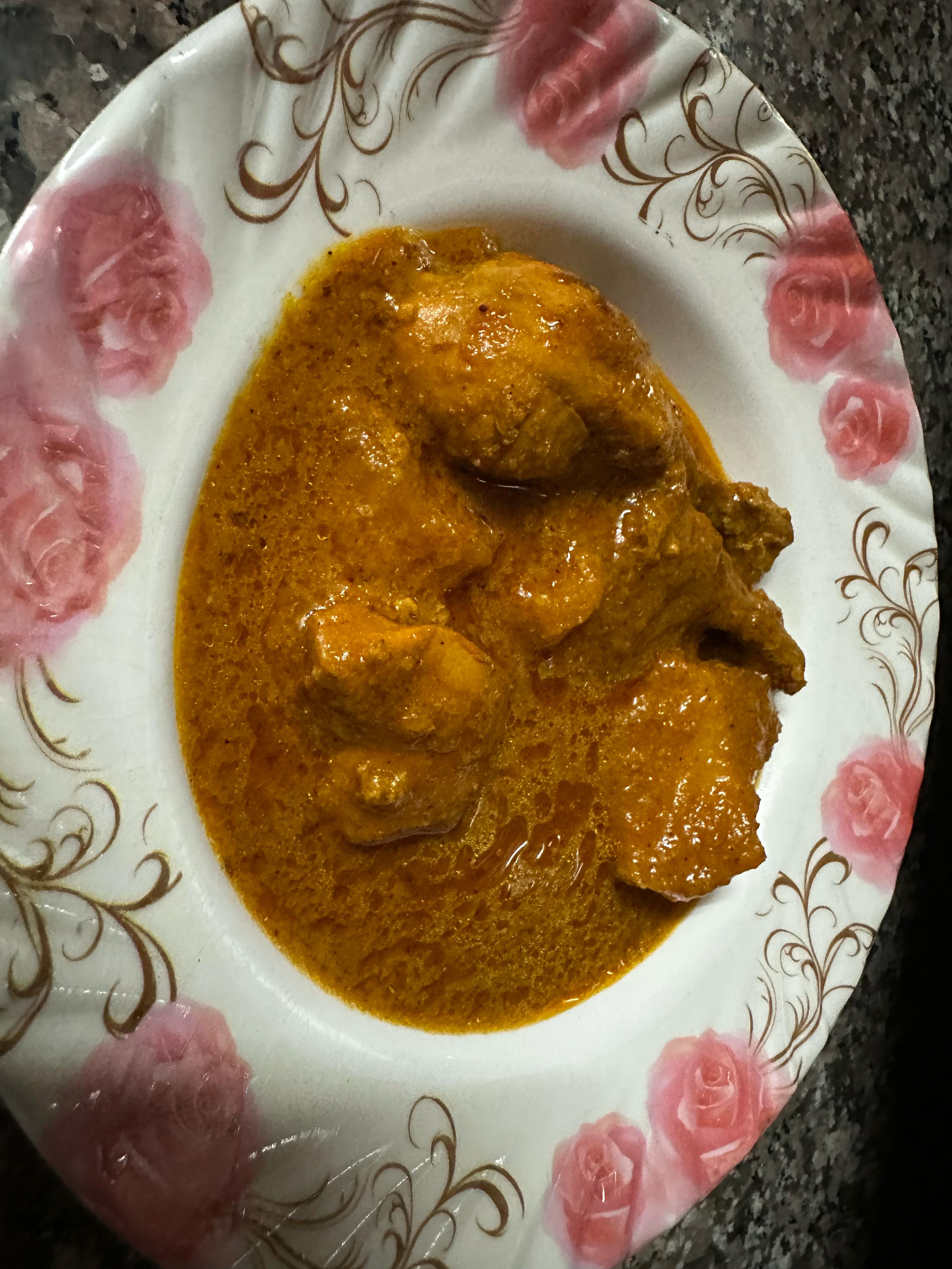 A plate of red chicken curry on a rose-patterned plate